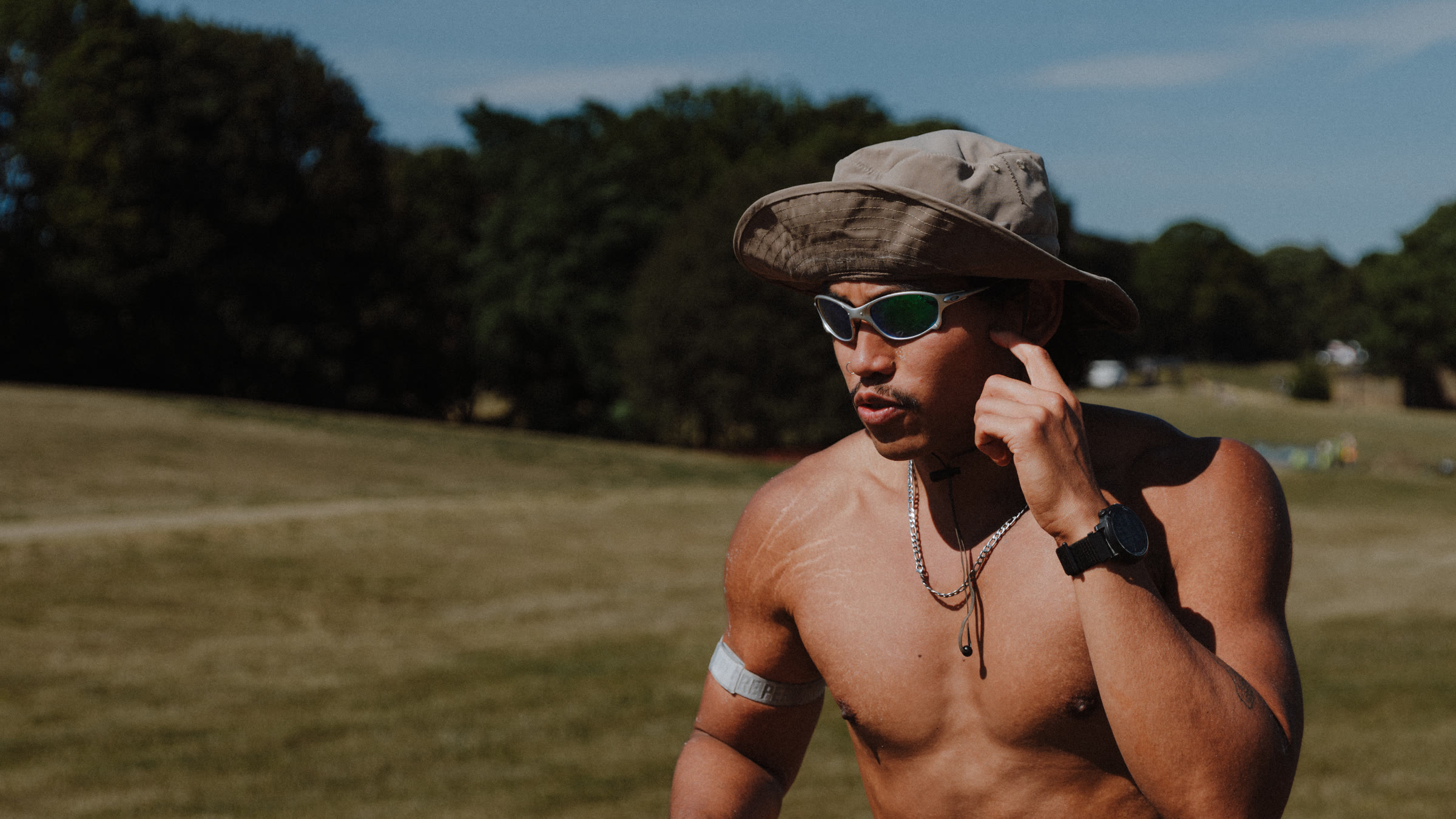 A runner mid-race in a bucket hat and mirrored sunglasses, crossing sunlit open parkland